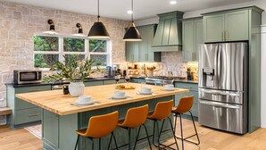 A kitchen with a large island, bar stools, a stainless steel refrigerator, and green cabinets. - Luxury MTN Retreat | Hot Tub | Fire Pit | Game Rm (Fleetwood)