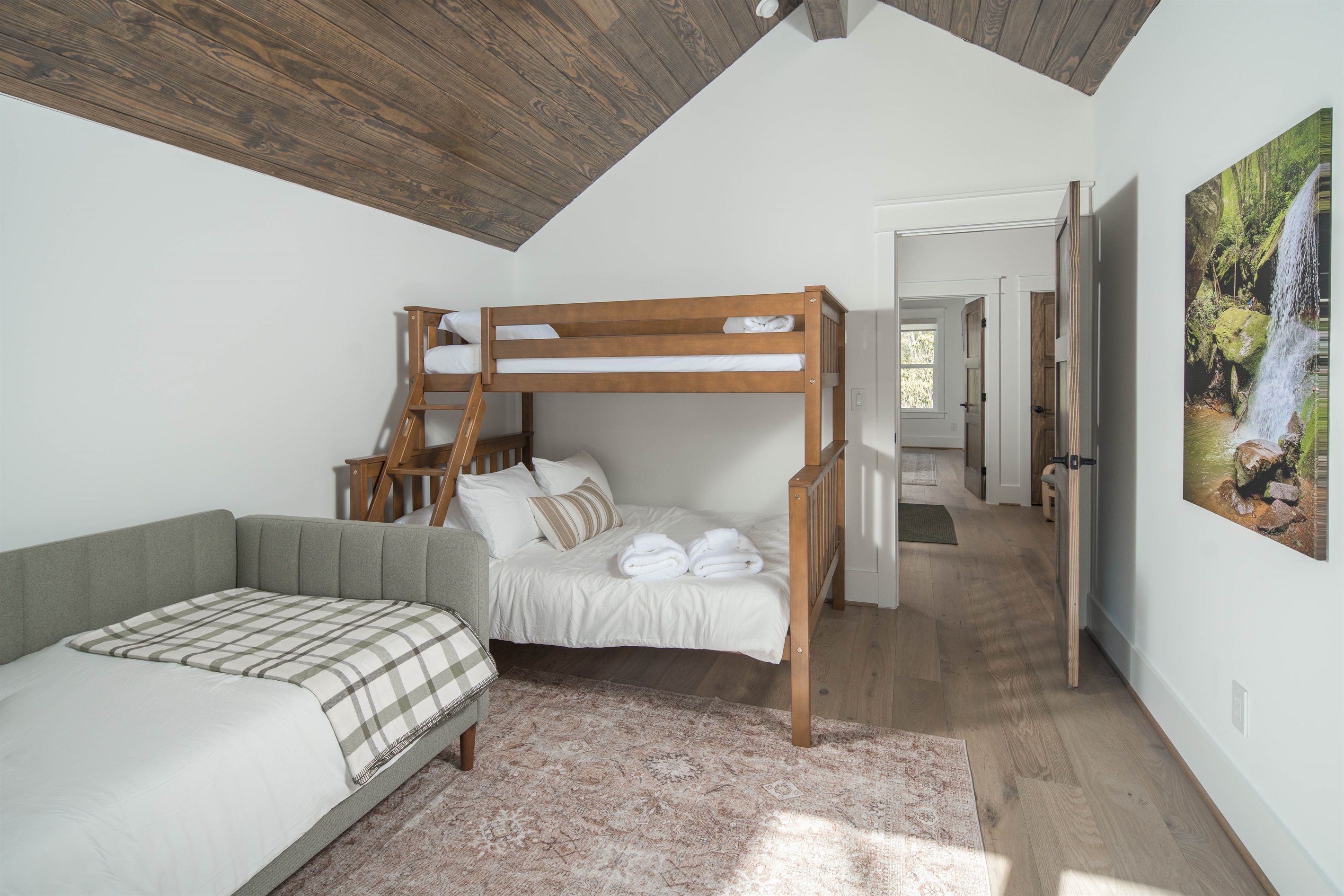 Un dormitorio con una cama nido, un sofá cama, un tapete estampado y un cuadro de una cascada.