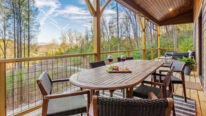 A covered outdoor patio with a wooden table, chairs, and a dining set. - Luxury MTN Retreat | Hot Tub | Fire Pit | Game Rm (Fleetwood)