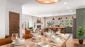 A dining area with a long table set for a meal, a kitchen in the background, and a stone wall. - Luxury MTN Retreat | Hot Tub | Fire Pit | Game Rm (Fleetwood)