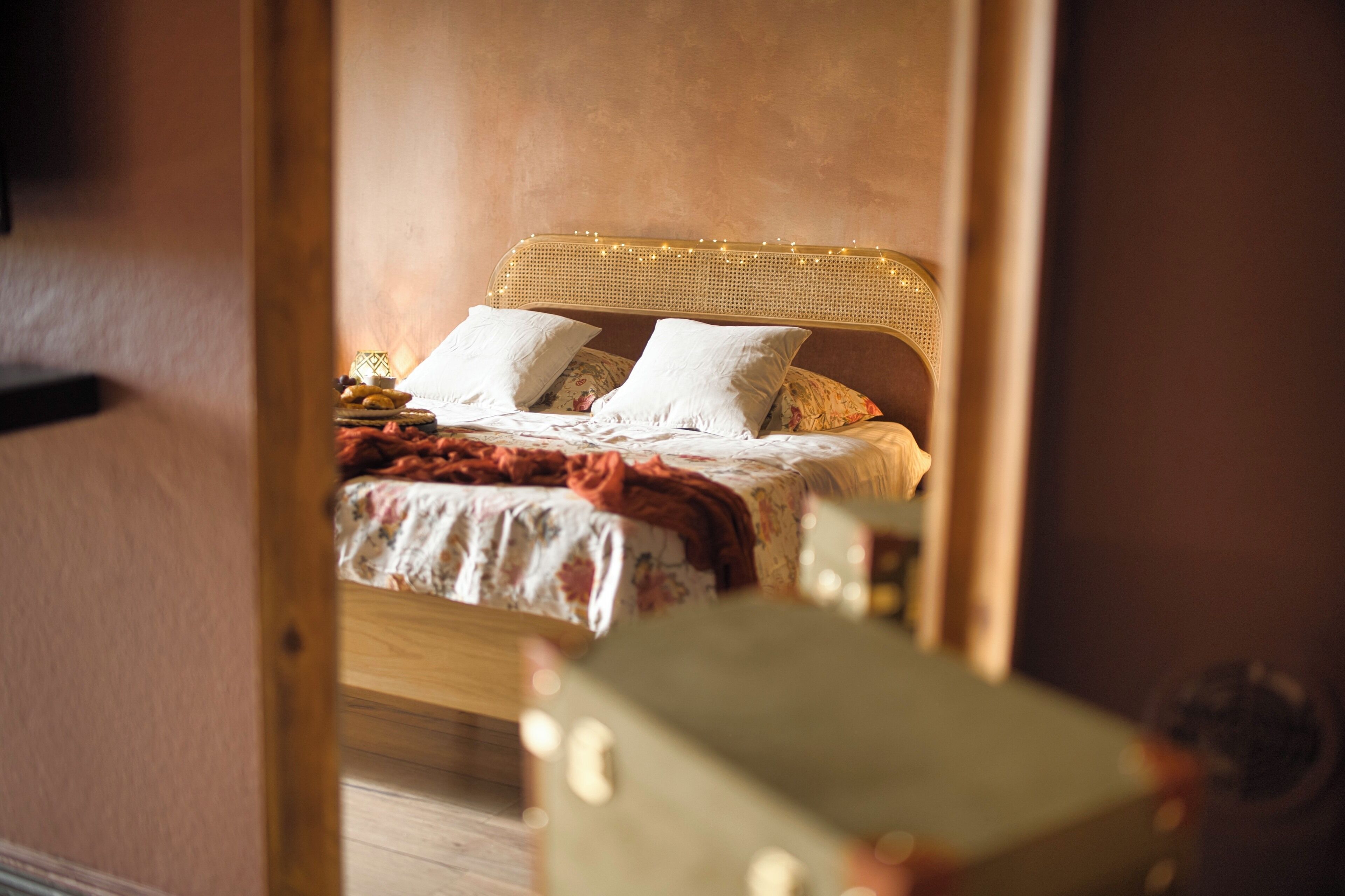 Un dormitorio con cabecera de madera, colcha estampada y manta roja.
