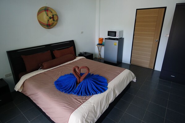 A neatly made bed with a swan-shaped towel arrangement, a microwave, and a refrigerator in a hotel room. - Lotus Bleu Resort & Restaurant (Rawai)
