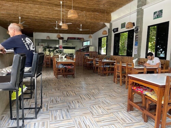 A restaurant with wooden flooring, tables, chairs, and hanging lights. - Lotus Bleu Resort & Restaurant (Rawai)