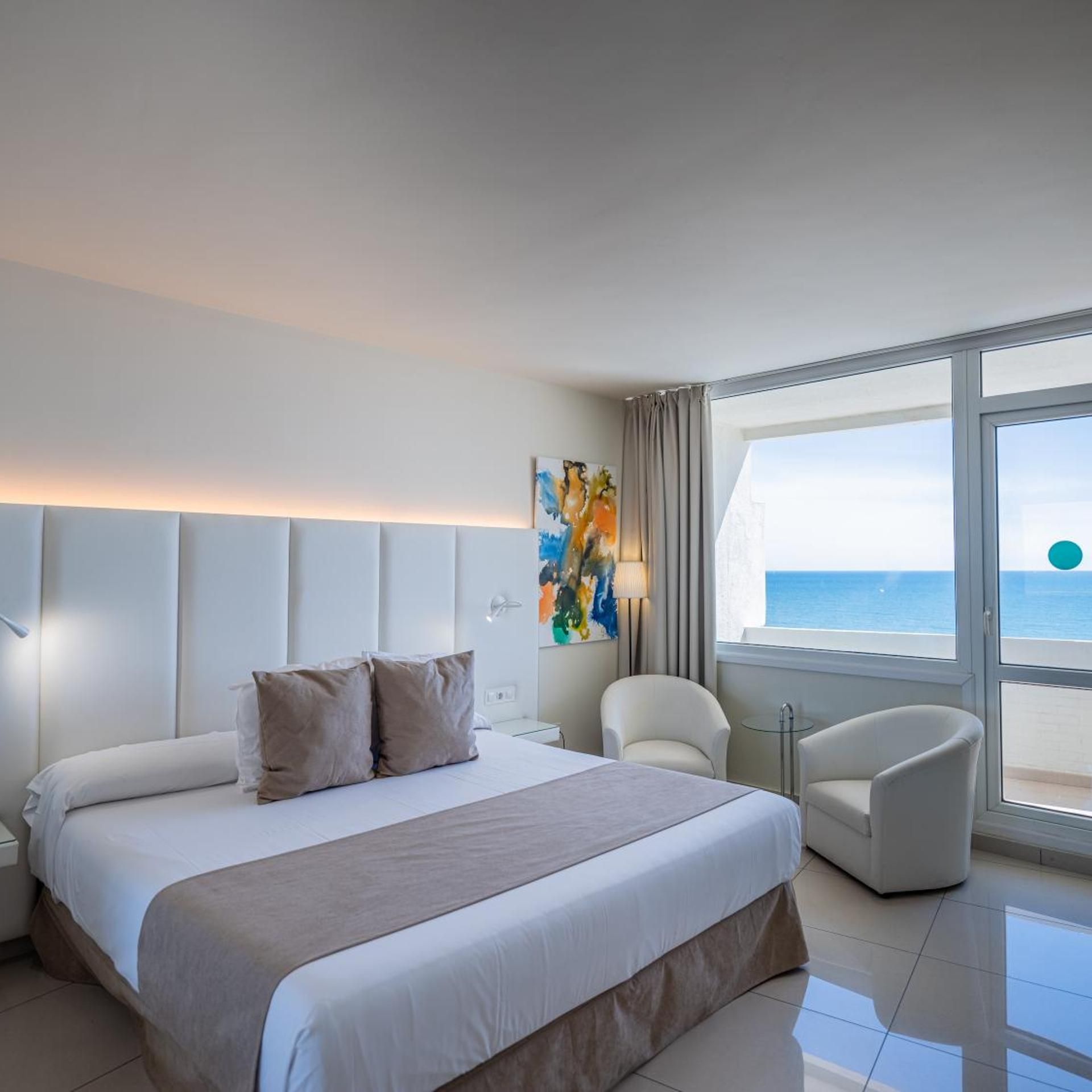 Habitación de hotel moderna con una cama grande, zona de estar y vista al mar.