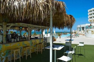 Un bar en la playa con techo de paja, mesas al aire libre y vistas al océano.