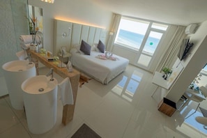 A modern hotel room with a large bed, two white sinks, a vanity with a mirror, and a view of the ocean. - On Hotels Oceanfront Adults Designed (Almonte)