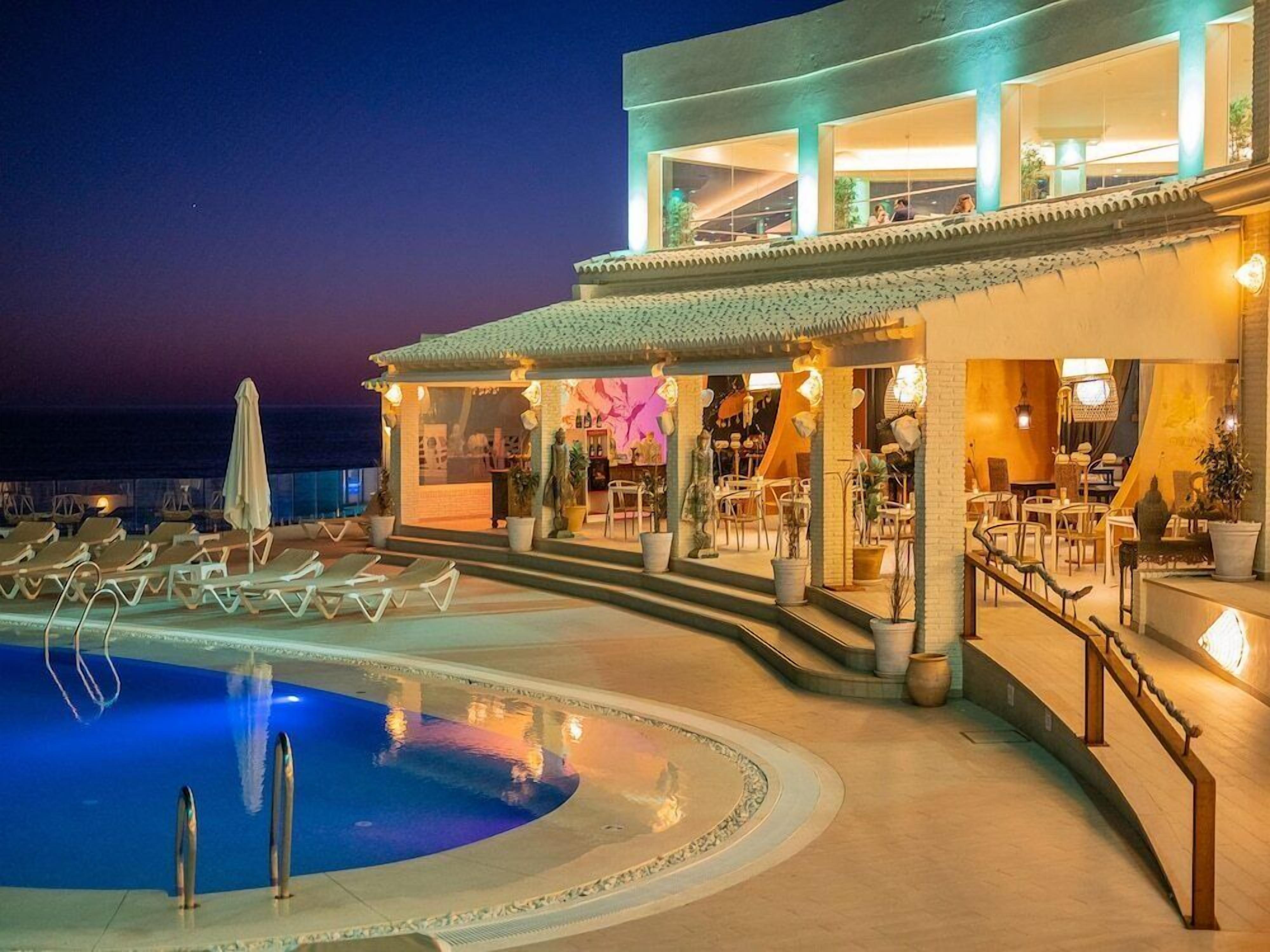 A hotel with a swimming pool, outdoor seating, and a bar area.