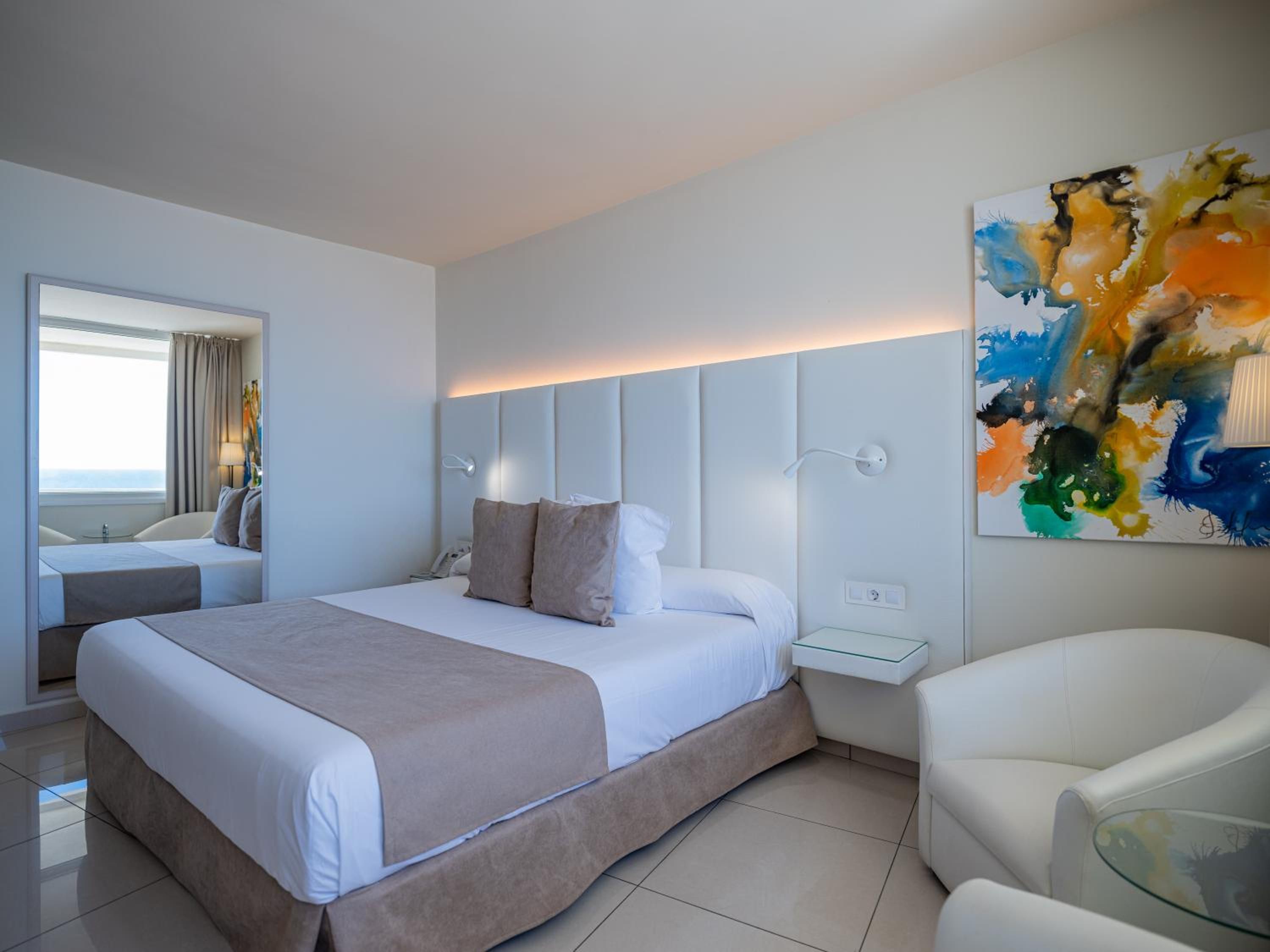 Una habitación de hotel moderna con una cama grande, una mesita de noche, una silla y un cuadro en la pared.