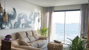 A modern living room with a beige sofa, a round wooden coffee table, and a large abstract painting on the wall. - On Hotels Oceanfront Adults Designed (Almonte)