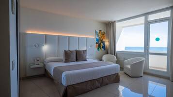 Habitación de hotel moderna con una cama grande, una mesita de noche con teléfono, una silla y vista al mar.