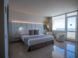 Habitación de hotel moderna con una cama grande, una mesita de noche con teléfono, una silla y vista al mar.