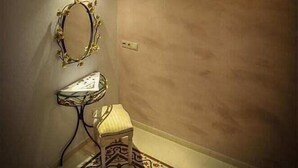 A room with a patterned rug, a small stool, a wall-mounted mirror, and a ceiling light fixture. - Villa Amalia (Rhodes)
