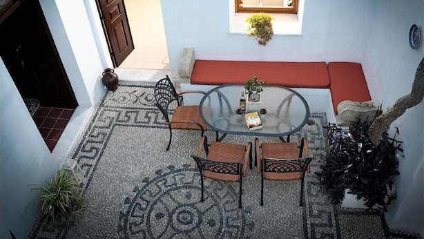 A patio area with a round glass table, four chairs, a red cushioned bench, and a potted plant. - Villa Amalia (Rhodes)