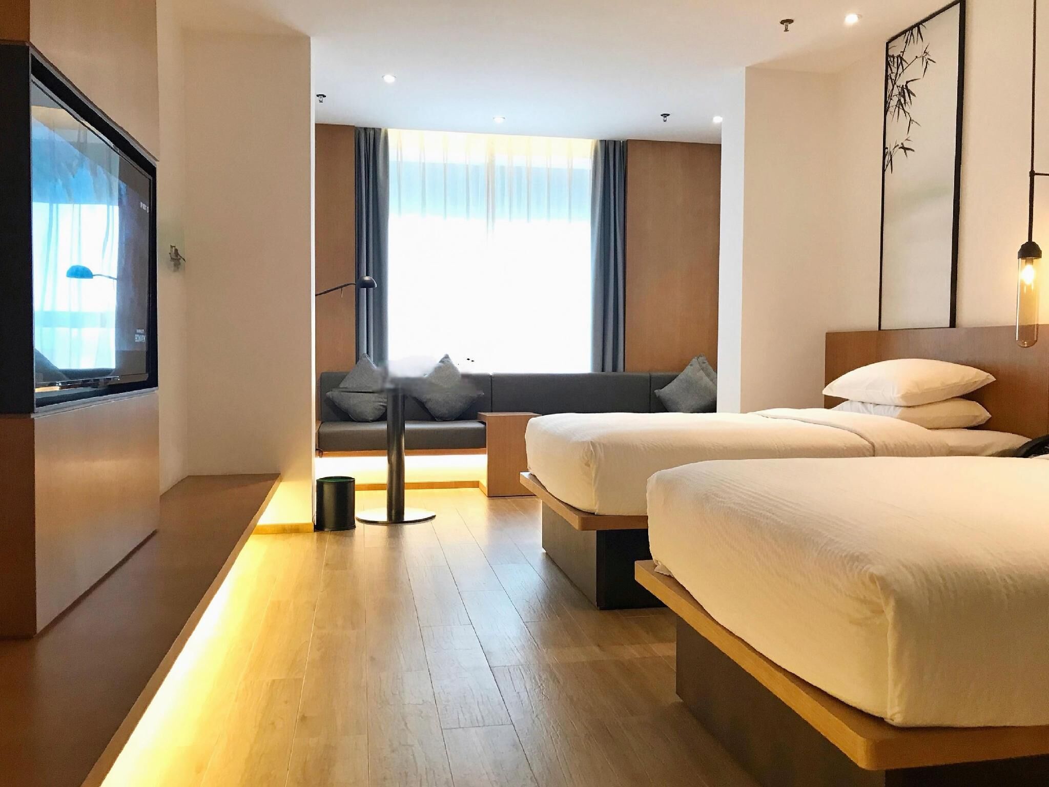Una camera d'albergo moderna con due letti, un divano, una TV e un'ampia finestra con tende.