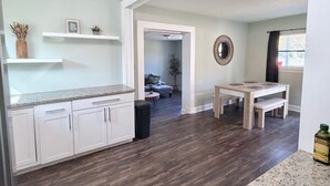 Een moderne keuken met witte kasten, een granieten aanrechtblad en een eethoek met een houten tafel en bank.