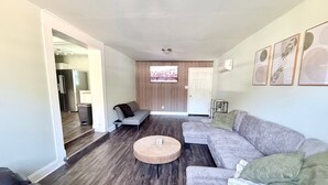 Een moderne woonkamer met een grijze bank, een ronde salontafel en een donker houten vloer.