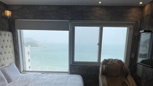 Ett sovrum med en säng, en massagefåtölj och ett stort fönster med utsikt över havet.