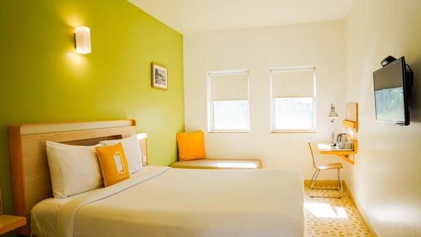 A hotel room with a bed, a desk, a chair, a TV, and two windows. - Bloomrooms @ Calangute (Candolim)