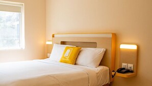 A hotel room with a bed, a bedside table with a phone, and a window. - Bloomrooms @ Calangute (Candolim)