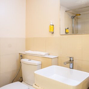 A bathroom with a toilet, sink, and a hand wash dispenser. - Bloomrooms @ Calangute (Candolim)