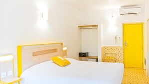 A hotel room with a bed, bedside table, lamp, mirror, wardrobe, and a yellow door. - Bloomrooms @ Calangute (Candolim)