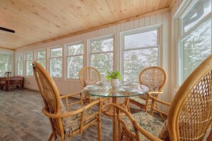 A dining area with wicker chairs and a glass table, large windows, and a wooden ceiling. - Waterfront on Butterfly Lake l Hottub l Firepit (Port Carling)