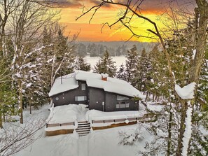 Una cabaña con tejado cubierto de nieve, rodeada de árboles y un paisaje nevado.