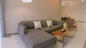 A modern living room with a sectional sofa, a coffee table, and a floor lamp. - The Landmark Studio Suite (George Town)