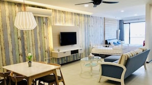 A modern living room with a flat-screen TV, a dining table with chairs, a sofa, and a ceiling fan. - The Landmark Studio Suite (George Town)