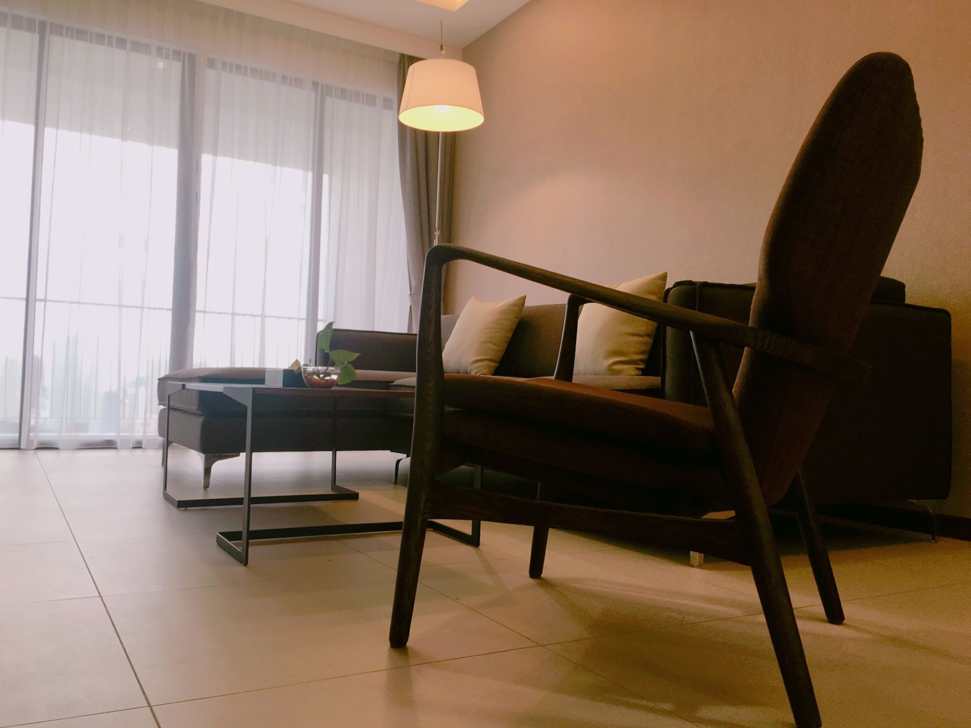 A modern living room with a dark brown sofa, a glass coffee table, and a lamp.