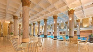 Amplio espacio interior con piscina, rodeado de columnas con diseños elaborados, y amueblado con sillas y mesas a rayas.