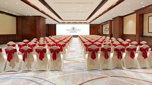Un salón de conferencias con filas de sillas blancas con cintas rojas, una pantalla grande al frente y un panel de pared de madera.