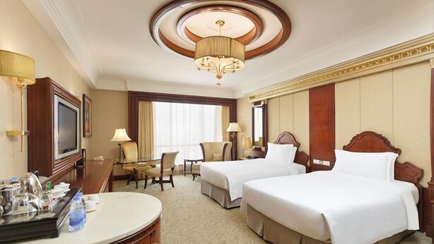 Habitación de hotel con dos camas, un escritorio, televisión y candelabro.