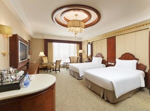 A hotel room with two beds, a desk, a television, and a chandelier. - Regal Palace Hotel (Dongguan)