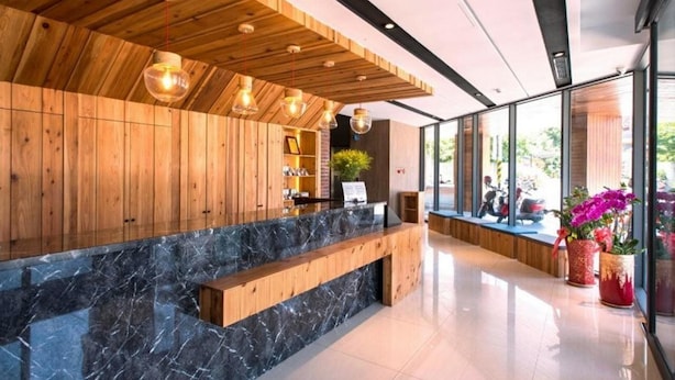 A modern reception area with wooden paneling, a marble counter, and a view of the outdoors through large windows. - Traveller-inn Tiehua Cultural and Creative Hotel (Taitung)
