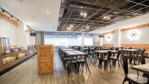 A spacious dining area with multiple tables and chairs, wooden flooring, and a modern ceiling design. - Traveller-inn Tiehua Cultural and Creative Hotel (Taitung)