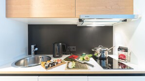 A modern kitchen with a stainless steel sink, a kettle, a pot, and various food items including sushi. - Smartment Business Berlin Karlshorst (Berlin)