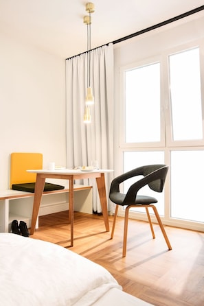 Een moderne slaapkamer met een houten bed, een bureau met een gele stoel, een zwarte stoel en een groot raam met gordijnen.