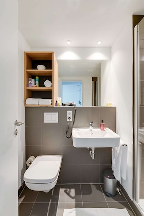 A compact bathroom with a shower, toilet, and a small shelf with toiletries. - Smartment Business Berlin Karlshorst (Berlin)