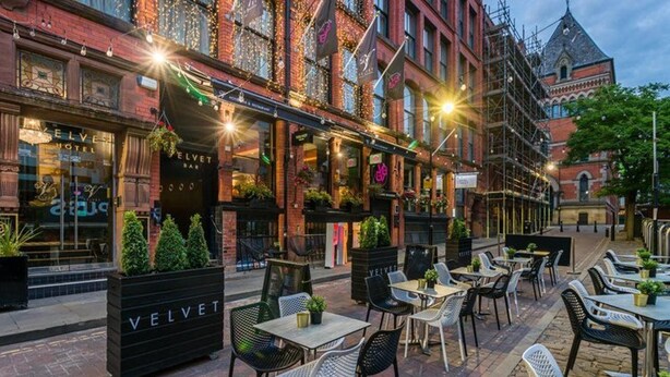 An outdoor seating area with tables and chairs, a sign for 'VELVET HOTEL', and a building with brick facade and windows. - Velvet Hotel Manchester, Worldhotels Crafted (Manchester)