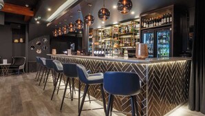 A bar with a modern design, featuring a herringbone patterned wall, a bar counter with stools, and a variety of bottles and glasses. - Velvet Hotel Manchester, Worldhotels Crafted (Manchester)