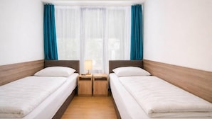 A hotel room with two single beds, a wooden headboard, a nightstand with a lamp, and a window with blue curtains. - Absolut City Hostel Budapest (Budapest)