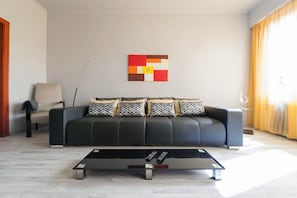 Una sala de estar moderna con un sofá de cuero negro, una mesa de centro de vidrio y un cuadro abstracto contemporáneo en la pared.