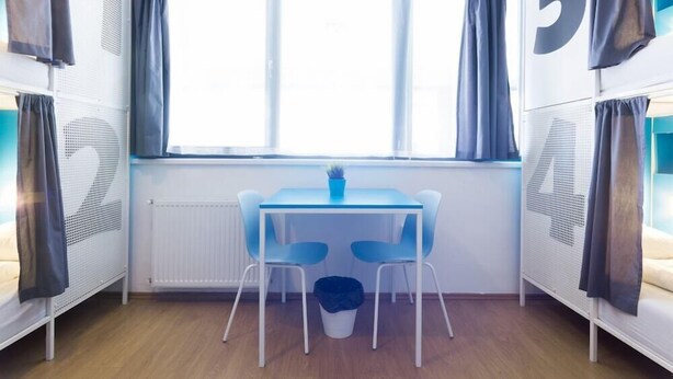 A room with bunk beds, a window with curtains, a table with chairs, and a radiator. - Absolut City Hostel Budapest (Budapest)
