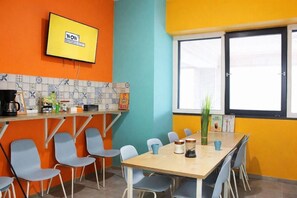 Una habitación de colores vivos con un televisor montado en la pared, un salpicadero de azulejos y una ventana con persianas.