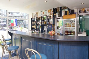 Una zona de bar con mostrador, taburetes y estantes llenos de botellas.