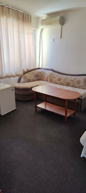 Una sala de estar con un sofá, una mesita, un refrigerador y un equipo de aire acondicionado en la pared.
