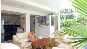A hotel lobby with a reception desk, a change of currency sign, and a glass-enclosed exchange counter.