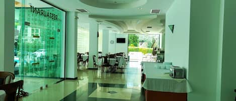 Um restaurante com parede de vidro, mesas, cadeiras e vista para o exterior.