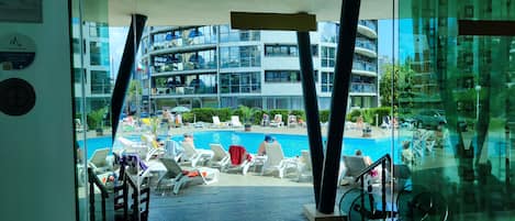 A modern building with a pool area, including lounge chairs and umbrellas.
